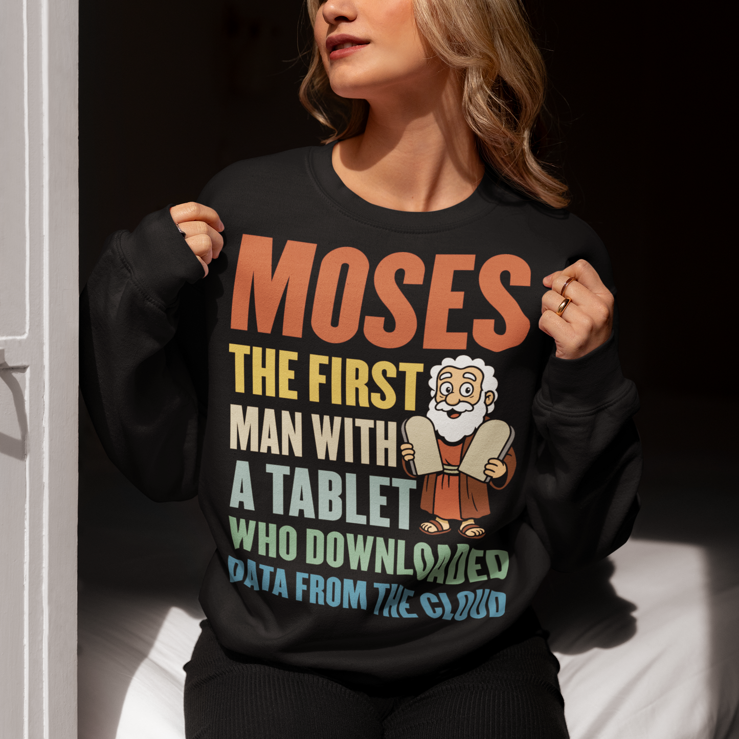 Black sweatshirt featuring a humorous graphic of Moses holding stone tablets with colorful text that reads “Moses the first man with a tablet who downloaded data from the cloud.” The design uses a playful, retro style with multicolored lettering and a cartoon illustration, combining biblical imagery with modern tech humor.
