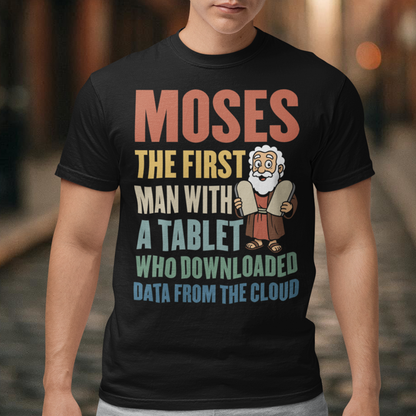 Black t-shirt featuring a humorous graphic of Moses holding stone tablets with colorful text that reads “Moses the first man with a tablet who downloaded data from the cloud.” The design uses a playful, retro style with multicolored lettering and a cartoon illustration, combining biblical imagery with modern tech humor.