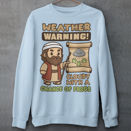 Light Blue sweatshirt featuring a cute cartoon Moses pointing at a weather scroll that shows a smiling rain cloud and falling frogs. The text reads “Weather Warning! Cloudy With a Chance of Frogs.” The design uses playful retro colors with funny biblical humor inspired by the plague of frogs story.
