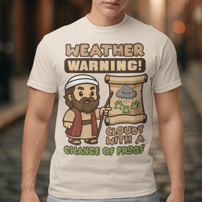 Beige t-shirt featuring a cute cartoon Moses pointing at a weather scroll that shows a smiling rain cloud and falling frogs. The text reads “Weather Warning! Cloudy With a Chance of Frogs.” The design uses playful retro colors with funny biblical humor inspired by the plague of frogs story