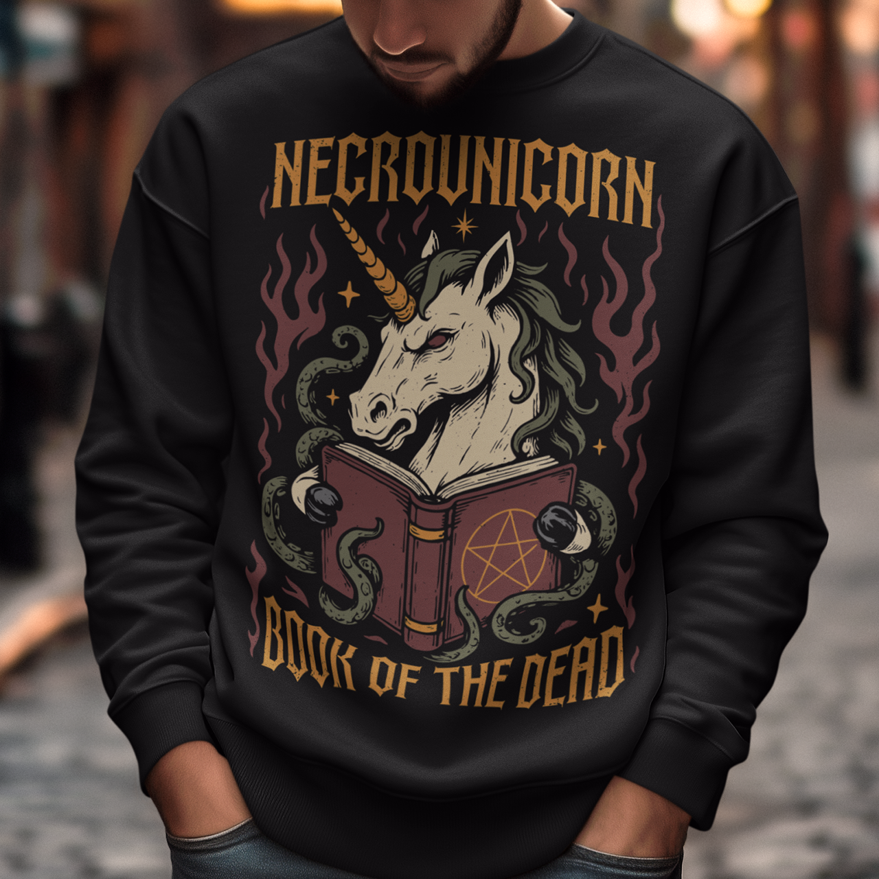 Black sweatshirt featuring a dark fantasy graphic of an evil unicorn reading a spellbook with a pentagram symbol. The design includes flames, tentacles, stars, and gothic lettering reading “Necrounicorn” and “Book of the Dead.” Spooky occult-inspired artwork with horror, witchcore, and fantasy aesthetics.