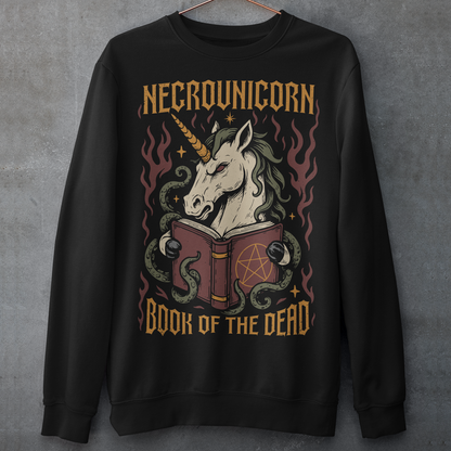 Black sweatshirt featuring a dark fantasy graphic of an evil unicorn reading a spellbook with a pentagram symbol. The design includes flames, tentacles, stars, and gothic lettering reading “Necrounicorn” and “Book of the Dead.” Spooky occult-inspired artwork with horror, witchcore, and fantasy aesthetics.