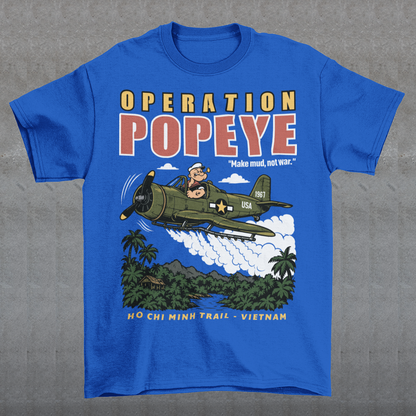 Blue T-shirt featuring a retro cartoon-style Popeye flying a vintage military aircraft over a lush Vietnam jungle landscape. The design reads “OPERATION POPEYE” with the phrase “Make mud, not war” and “HO CHI MINH TRAIL - VIETNAM.” A bold graphic inspired by Vietnam War history, aviation, military culture, and classic cartoon art.