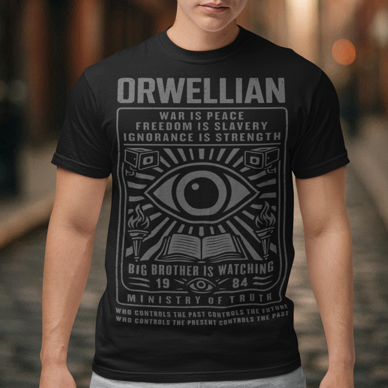 This black shirt channels the unsettling spirit of George Orwell’s 1984 with bold, high-contrast artwork and iconic slogans that refuse to whisper. The all-seeing eye dominates the design, flanked by surveillance cameras, burning torches, and an open book, a visual chorus of control, truth, and resistance. Phrases like “War Is Peace,” “Freedom Is Slavery,” and “Ignorance Is Strength” sit beneath the unmistakable warning: Big Brother Is Watching.