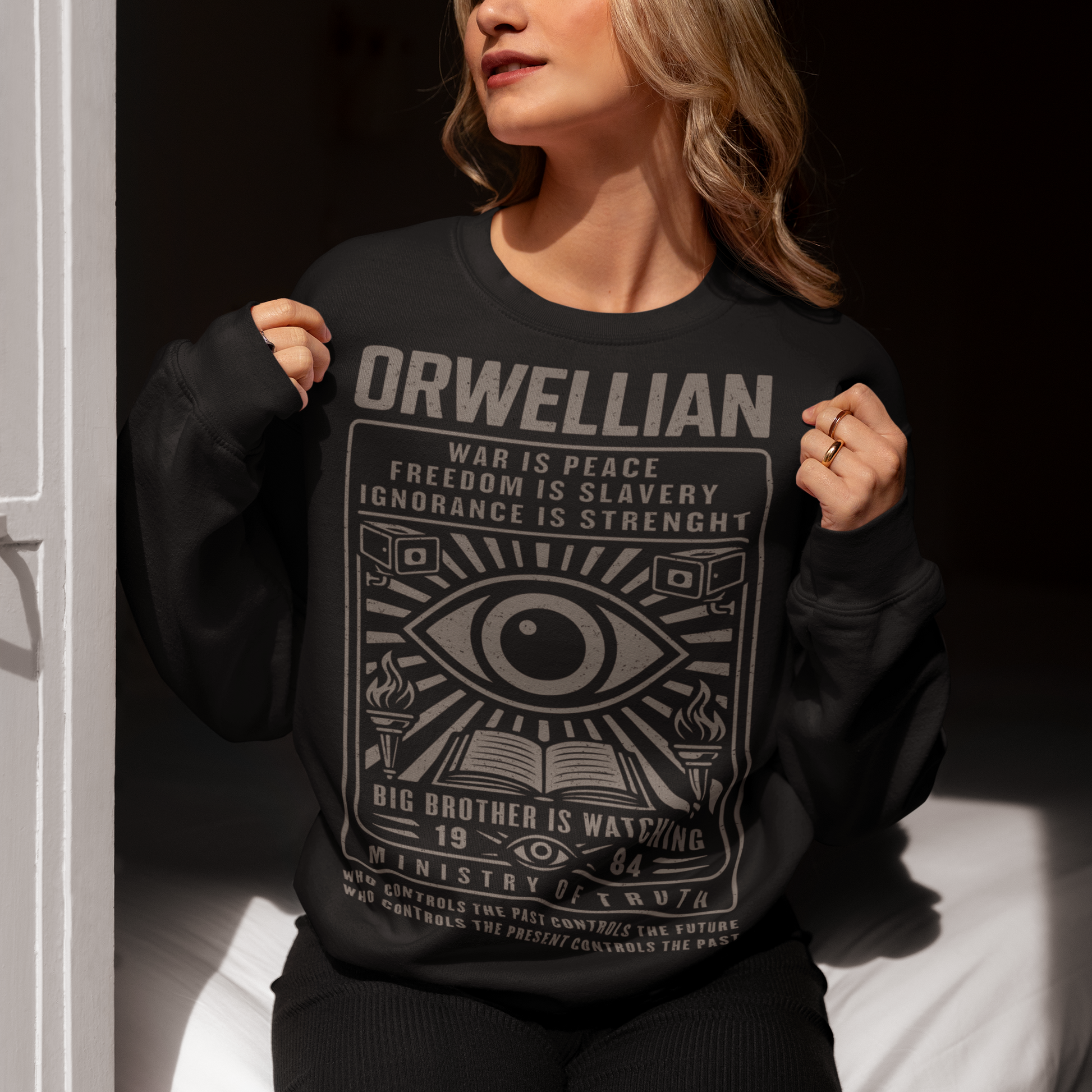 This black Sweatshirt channels the unsettling spirit of George Orwell’s 1984 with bold, high-contrast artwork and iconic slogans that refuse to whisper. The all-seeing eye dominates the design, flanked by surveillance cameras, burning torches, and an open book, a visual chorus of control, truth, and resistance. Phrases like “War Is Peace,” “Freedom Is Slavery,” and “Ignorance Is Strength” sit beneath the unmistakable warning: Big Brother Is Watching.
