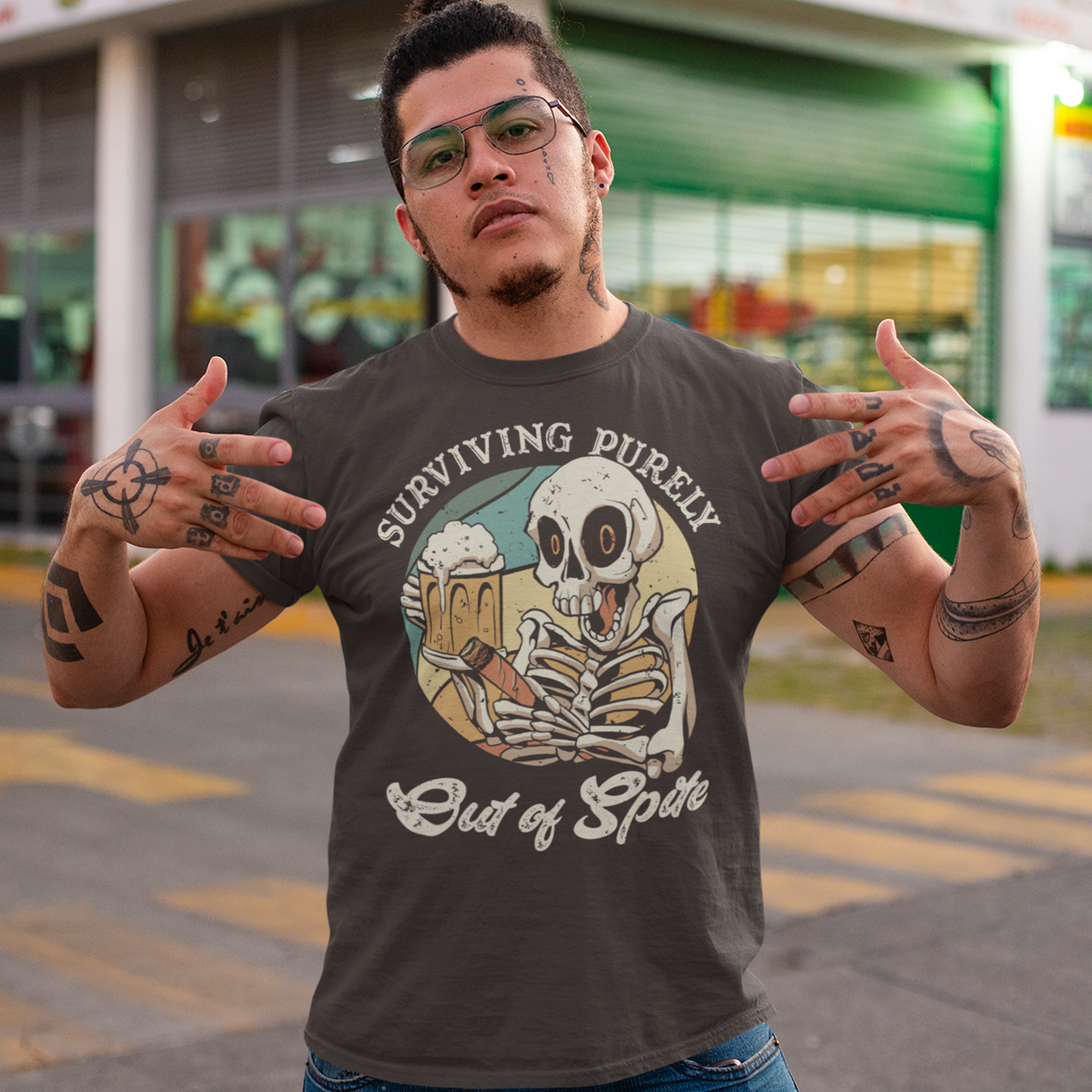 Brown t-shirt with skeleton drinking beer and holding a cigar with text "SURVIVING PURELY OUT OF SPITE".