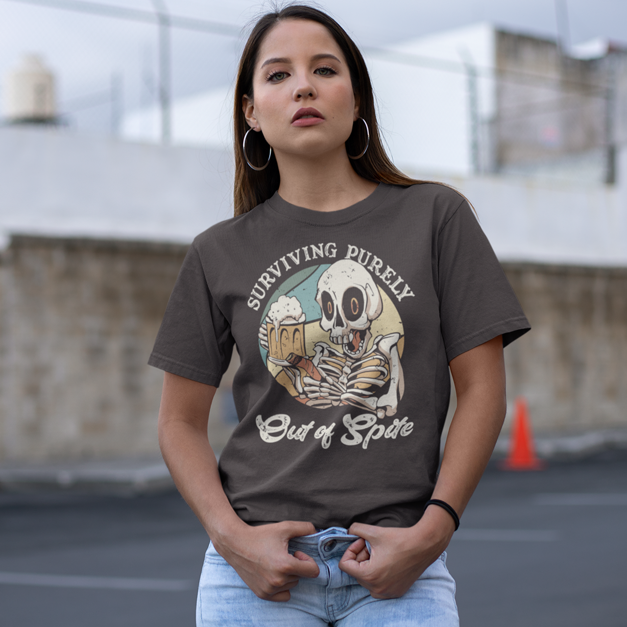 Brown t-shirt with skeleton drinking beer and holding a cigar with text "SURVIVING PURELY OUT OF SPITE".