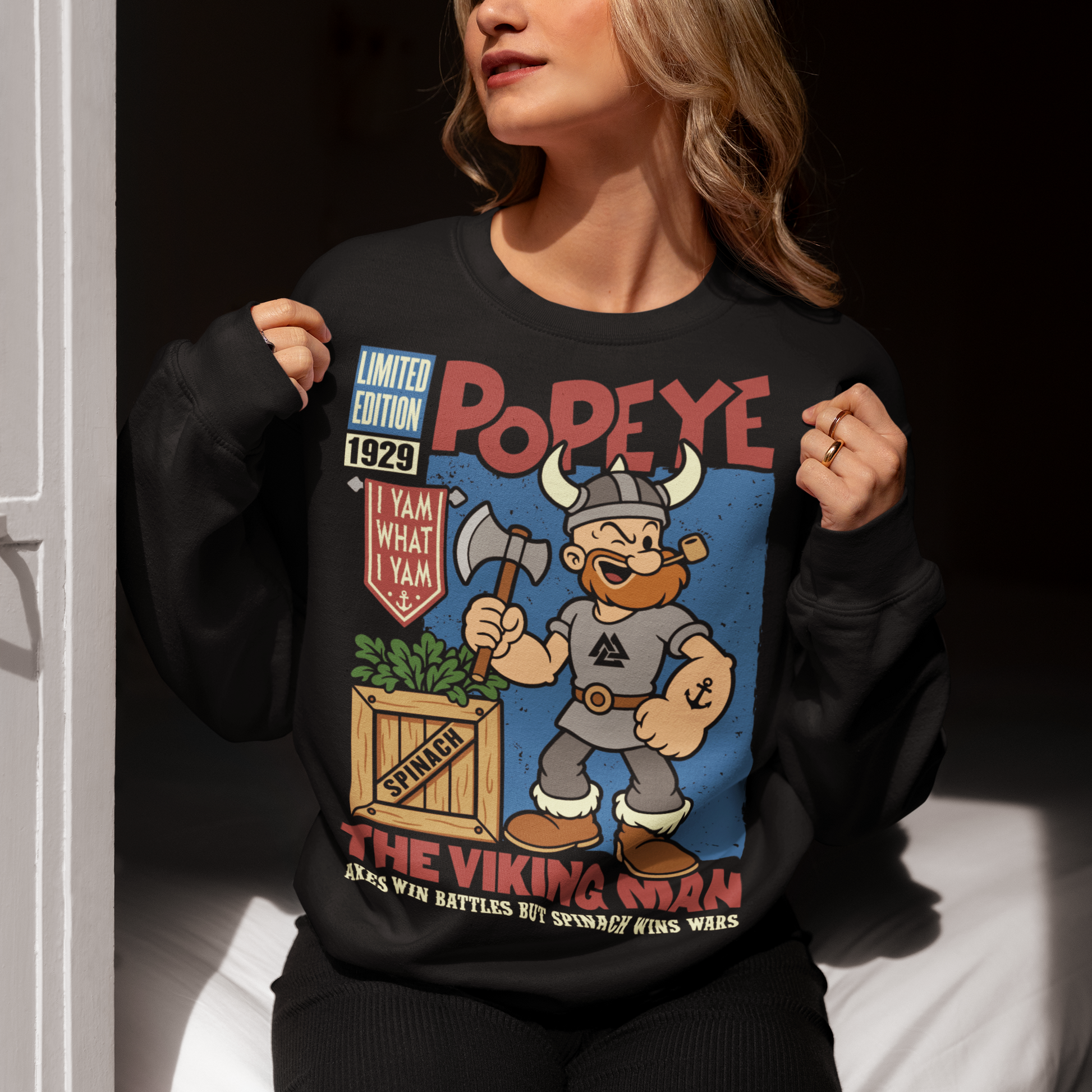 Channel old-school cartoon strength with this bold Popeye Viking graphic sweatshirt, where classic sailor swagger sails north into Viking territory. This playful design features a bearded Viking version of the legendary spinach-powered sailor, proudly gripping an axe beside a crate of spinach. With retro comic styling, vintage textures, and the iconic phrase “I Yam What I Yam,” the artwork celebrates the timeless humor and toughness that made the character famous.
