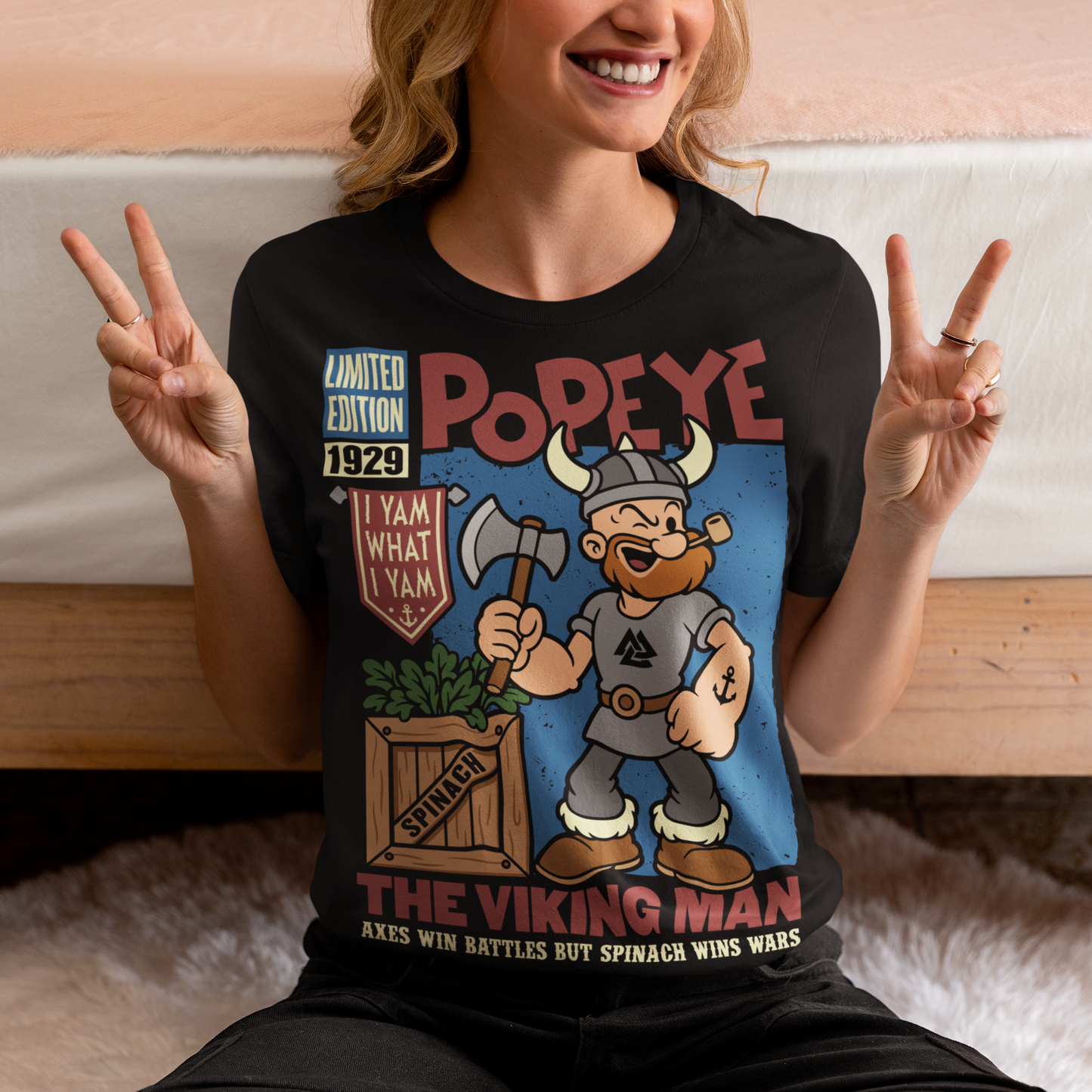 Channel old-school cartoon strength with this bold Popeye Viking graphic t-shirt, where classic sailor swagger sails north into Viking territory. This playful design features a bearded Viking version of the legendary spinach-powered sailor, proudly gripping an axe beside a crate of spinach. With retro comic styling, vintage textures, and the iconic phrase “I Yam What I Yam,” the artwork celebrates the timeless humor and toughness that made the character famous.
