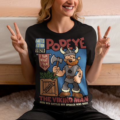 Channel old-school cartoon strength with this bold Popeye Viking graphic t-shirt, where classic sailor swagger sails north into Viking territory. This playful design features a bearded Viking version of the legendary spinach-powered sailor, proudly gripping an axe beside a crate of spinach. With retro comic styling, vintage textures, and the iconic phrase “I Yam What I Yam,” the artwork celebrates the timeless humor and toughness that made the character famous.
