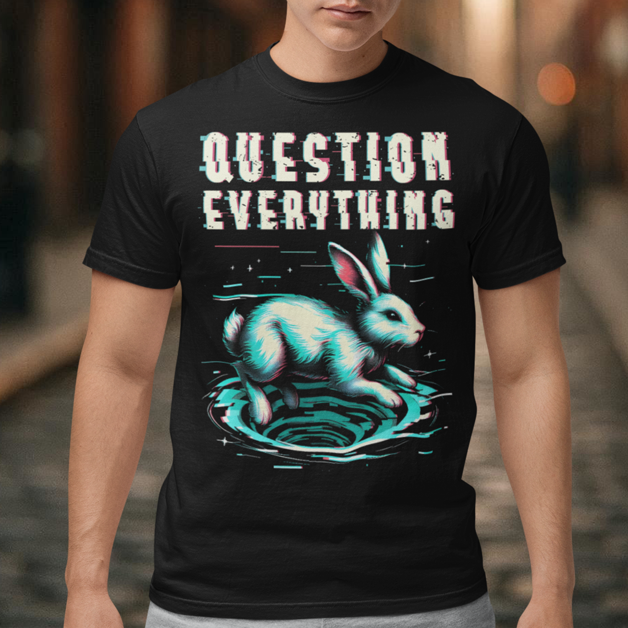A graphic t-shirt featuring a stylized illustration of a white rabbit diving headfirst into a swirling rabbit hole. The rabbit's legs and tail are visible as it disappears into the tunnel, surrounded by abstract, distorted digital effects. Above the image, the phrase "QUESTION EVERYTHING" appears in bold, glitched typography, as if corrupted or scrambled, adding a sense of mystery and rebellion. The design evokes curiosity and themes of exploration and truth-seeking.