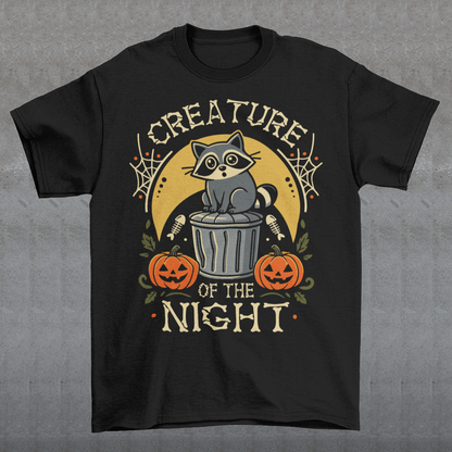 Black t-shirt featuring a vintage Halloween graphic of a cute raccoon sitting on a trash can beneath a golden moon. The design includes pumpkins, spider webs, leaves, fish bones, and distressed lettering reading “CREATURE OF THE NIGHT.” A spooky woodland animal design perfect for raccoon lovers, Halloween fans, and anyone who loves nocturnal creatures.