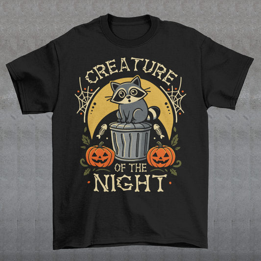 Black t-shirt featuring a vintage Halloween graphic of a cute raccoon sitting on a trash can beneath a golden moon. The design includes pumpkins, spider webs, leaves, fish bones, and distressed lettering reading “CREATURE OF THE NIGHT.” A spooky woodland animal design perfect for raccoon lovers, Halloween fans, and anyone who loves nocturnal creatures.