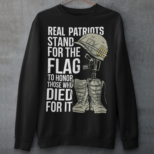 Sweatshirt design featuring a graphic of a military helmet resting on a rifle, which is standing upright in a pair of combat boots—a battlefield cross symbolizing fallen soldiers. Above and below the image is bold text that reads: "REAL PATRIOTS STAND FOR THE FLAG TO HONOR THOSE WHO DIED FOR IT." The design uses patriotic imagery to emphasize respect and remembrance for military service members who have sacrificed their lives.