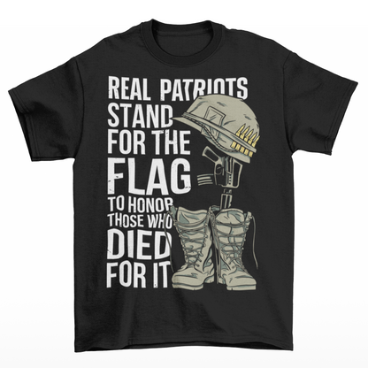 -shirt design featuring a graphic of a military helmet resting on a rifle, which is standing upright in a pair of combat boots—a battlefield cross symbolizing fallen soldiers. Above and below the image is bold text that reads: "REAL PATRIOTS STAND FOR THE FLAG TO HONOR THOSE WHO DIED FOR IT." The design uses patriotic imagery to emphasize respect and remembrance for military service members who have sacrificed their lives.
