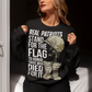 Sweatshirt design featuring a graphic of a military helmet resting on a rifle, which is standing upright in a pair of combat boots—a battlefield cross symbolizing fallen soldiers. Above and below the image is bold text that reads: "REAL PATRIOTS STAND FOR THE FLAG TO HONOR THOSE WHO DIED FOR IT." The design uses patriotic imagery to emphasize respect and remembrance for military service members who have sacrificed their lives.