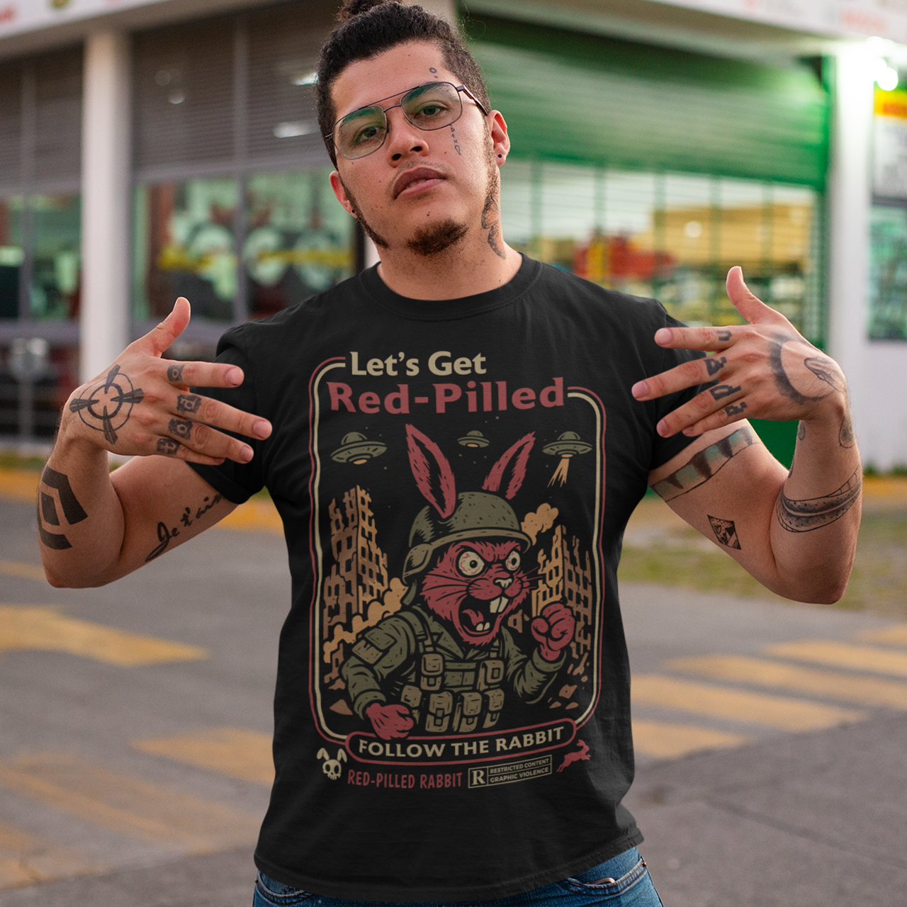 This black graphic tee dives headfirst down the rabbit hole. Featuring a fierce, red-eyed rabbit geared up like a rebel soldier, the design blends sci-fi paranoia, retro poster aesthetics, and counterculture attitude. Bold lettering reads “Let’s Get Red-Pilled” with “Follow the Rabbit” anchoring the scene, while crumbling cityscapes and hovering UFOs set a dystopian, mind-bending mood. This shirt feels like a lost propaganda poster from an alternate reality.