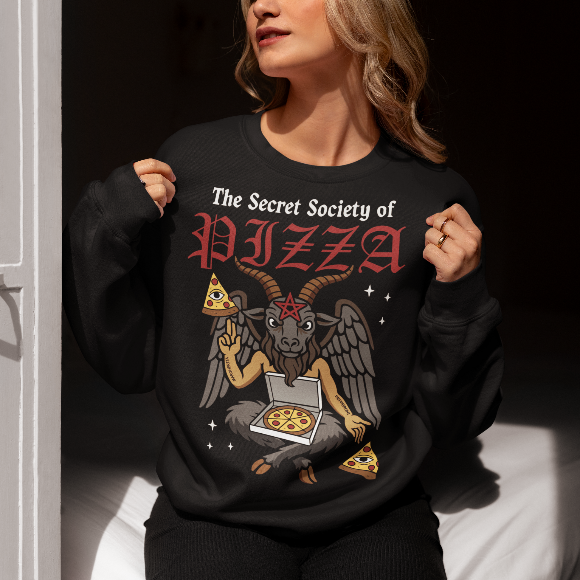 Black sweatshirt featuring a humorous occult-style design with the text “The Secret Society of Pizza.” Artwork shows a winged goat figure with horns and a pentagram holding pizza slices and an open pizza box, surrounded by small stars. Gothic lettering and playful dark humor create a spooky pizza-themed graphic tee design.