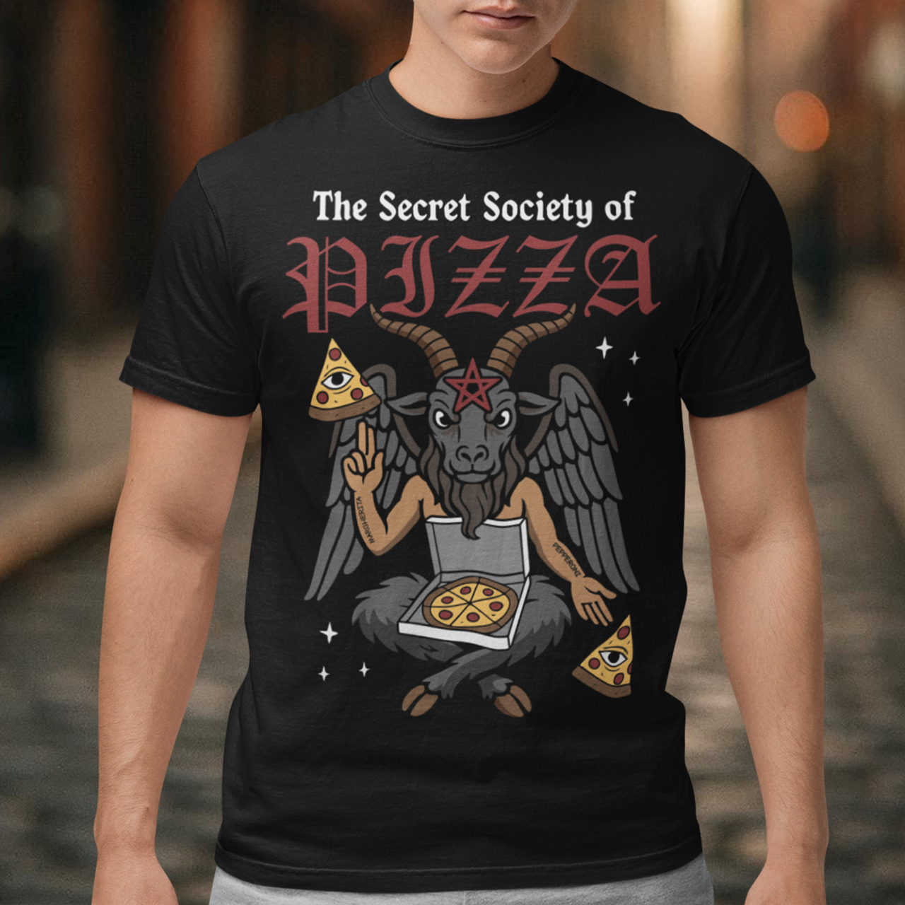 Black t-shirt featuring a humorous occult-style design with the text “The Secret Society of Pizza.” Artwork shows a winged goat figure with horns and a pentagram holding pizza slices and an open pizza box, surrounded by small stars. Gothic lettering and playful dark humor create a spooky pizza-themed graphic tee design.