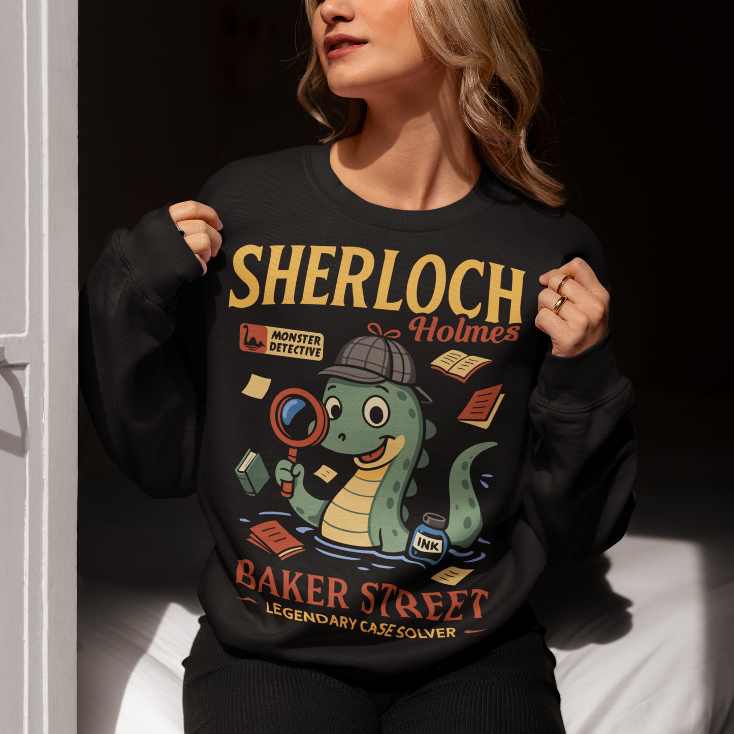 Meet the most curious creature on Baker Street with this fun and clever Sherloch Holmes Monster Detective sweatshirt. This playful design reimagines the legendary detective as an adorable little loch ness monster investigator, complete with a classic detective hat, magnifying glass, scattered case notes, and a bottle of ink ready to record the next big mystery. With its charming illustration style and witty wordplay, this shirt blends classic detective fiction with lighthearted monster humor.