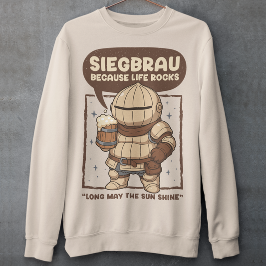 Beige sweatshirt featuring a cute, chibi-style armored knight Siegmeyer of Catarina holding a frothy beer mug. Above the character, bold text reads “Siegbrau because life rocks,” with smaller text below saying “Long may the sun shine.” The design has a playful fantasy theme with soft brown tones and a hand-drawn style, appealing to gamers and fans of medieval or RPG-inspired humor.