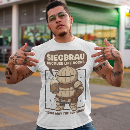 White t-shirt featuring a cute, chibi-style armored knight Siegmeyer of Catarina holding a frothy beer mug. Above the character, bold text reads “Siegbrau because life rocks,” with smaller text below saying “Long may the sun shine.” The design has a playful fantasy theme with soft brown tones and a hand-drawn style, appealing to gamers and fans of medieval or RPG-inspired humor.