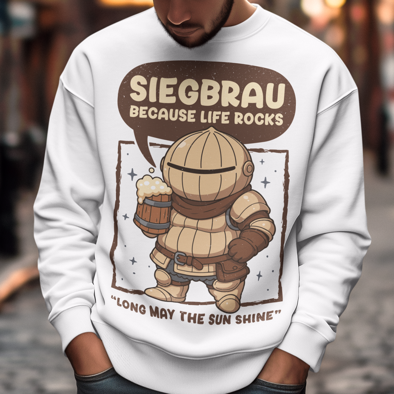 White sweatshirt featuring a cute, chibi-style armored knight Siegmeyer of Catarina holding a frothy beer mug. Above the character, bold text reads “Siegbrau because life rocks,” with smaller text below saying “Long may the sun shine.” The design has a playful fantasy theme with soft brown tones and a hand-drawn style, appealing to gamers and fans of medieval or RPG-inspired humor.