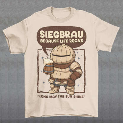 Beige t-shirt featuring a cute, chibi-style armored knight Siegmeyer of Catarina holding a frothy beer mug. Above the character, bold text reads “Siegbrau because life rocks,” with smaller text below saying “Long may the sun shine.” The design has a playful fantasy theme with soft brown tones and a hand-drawn style, appealing to gamers and fans of medieval or RPG-inspired humor.