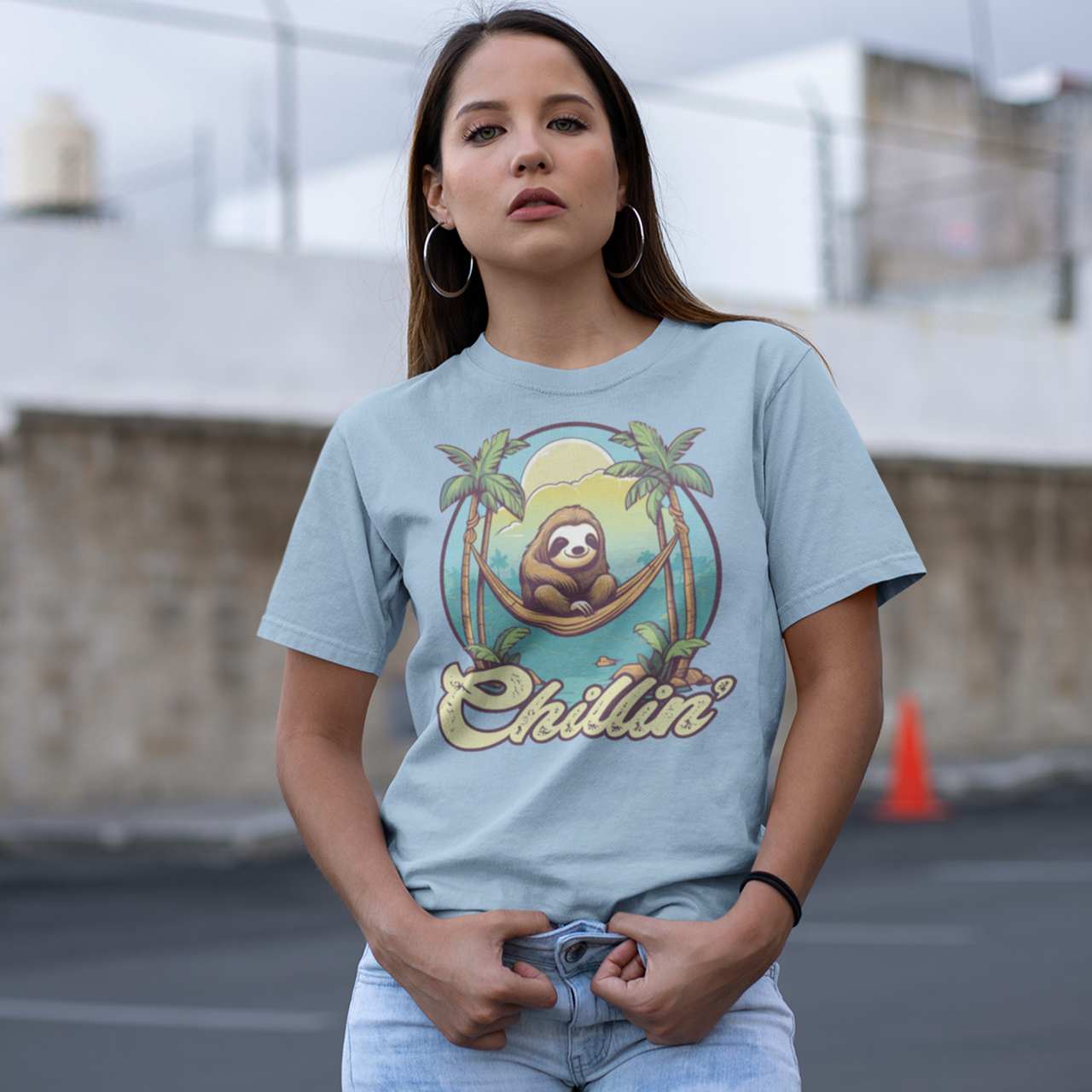 Light blue t-shirt of a sloth in a hammock on a beach with text "Chillin'".