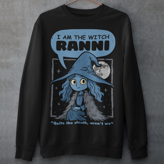 Black sweatshirt featuring a cute blue witch character with large eyes wearing a pointed hat and cloak, set against a night sky with a full moon and stars. Text above reads “I AM THE WITCH RANNI,” with a smaller quote below saying “Quite the sleuth, aren’t we.” The design has a dark fantasy, game-inspired style with soft blue tones and a whimsical, mystical aesthetic.