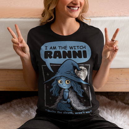 Black t-shirt featuring a cute blue witch character with large eyes wearing a pointed hat and cloak, set against a night sky with a full moon and stars. Text above reads “I AM THE WITCH RANNI,” with a smaller quote below saying “Quite the sleuth, aren’t we.” The design has a dark fantasy, game-inspired style with soft blue tones and a whimsical, mystical aesthetic.