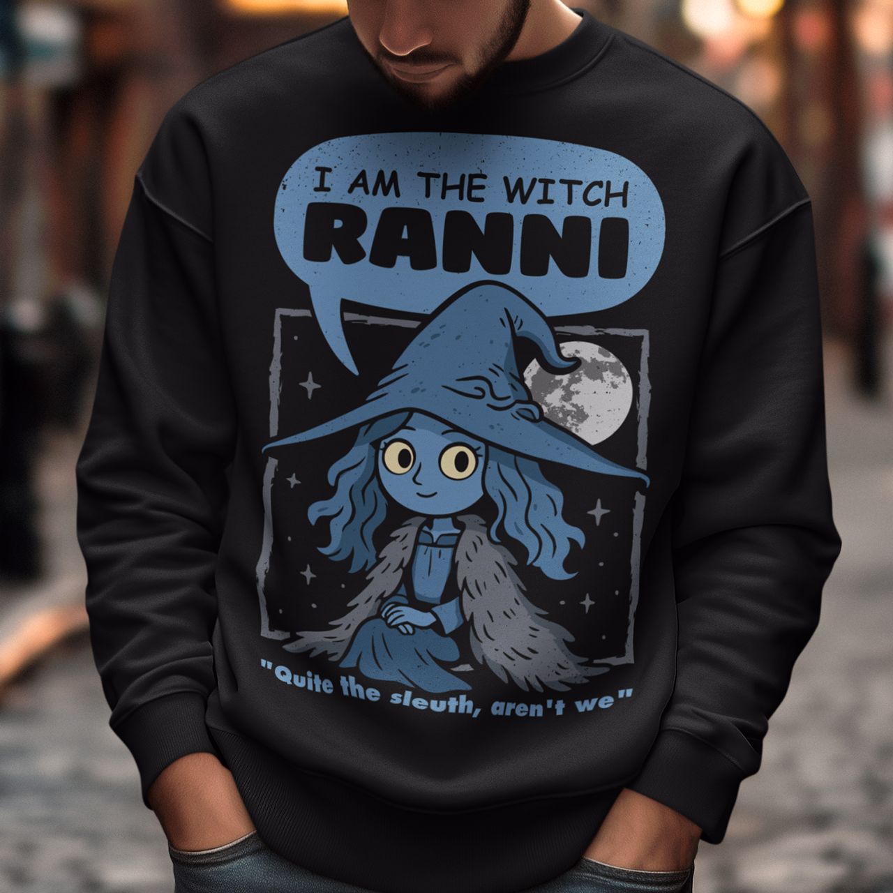 Black sweatshirt featuring a cute blue witch character with large eyes wearing a pointed hat and cloak, set against a night sky with a full moon and stars. Text above reads “I AM THE WITCH RANNI,” with a smaller quote below saying “Quite the sleuth, aren’t we.” The design has a dark fantasy, game-inspired style with soft blue tones and a whimsical, mystical aesthetic.