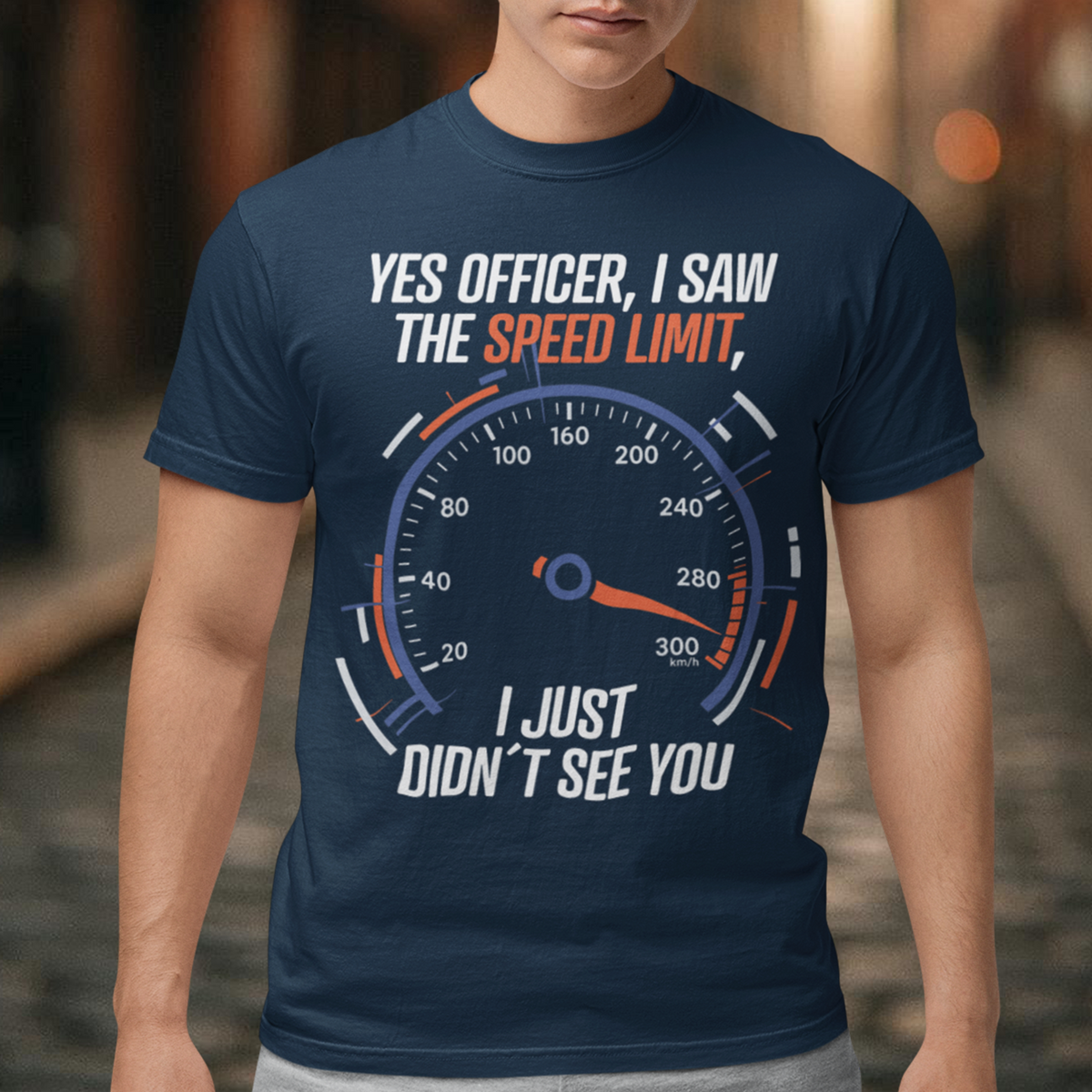 Navy blue t-shirt featuring a bold speedometer graphic with the text “YES OFFICER, I SAW THE SPEED LIMIT, I JUST DIDN’T SEE YOU.” The design uses white, orange, and blue lettering and accents, with a large speed gauge showing speeds up to 300 km/h. Funny driving and car enthusiast themed graphic.