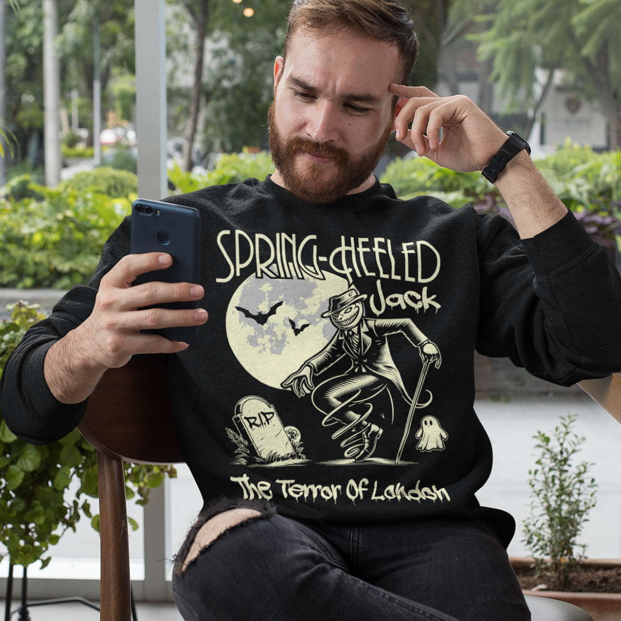 Black sweatshirt of Spring-heeled Jack beside a tombstone with a ghost on the other side. Text above SPRING-HEELED JACK.