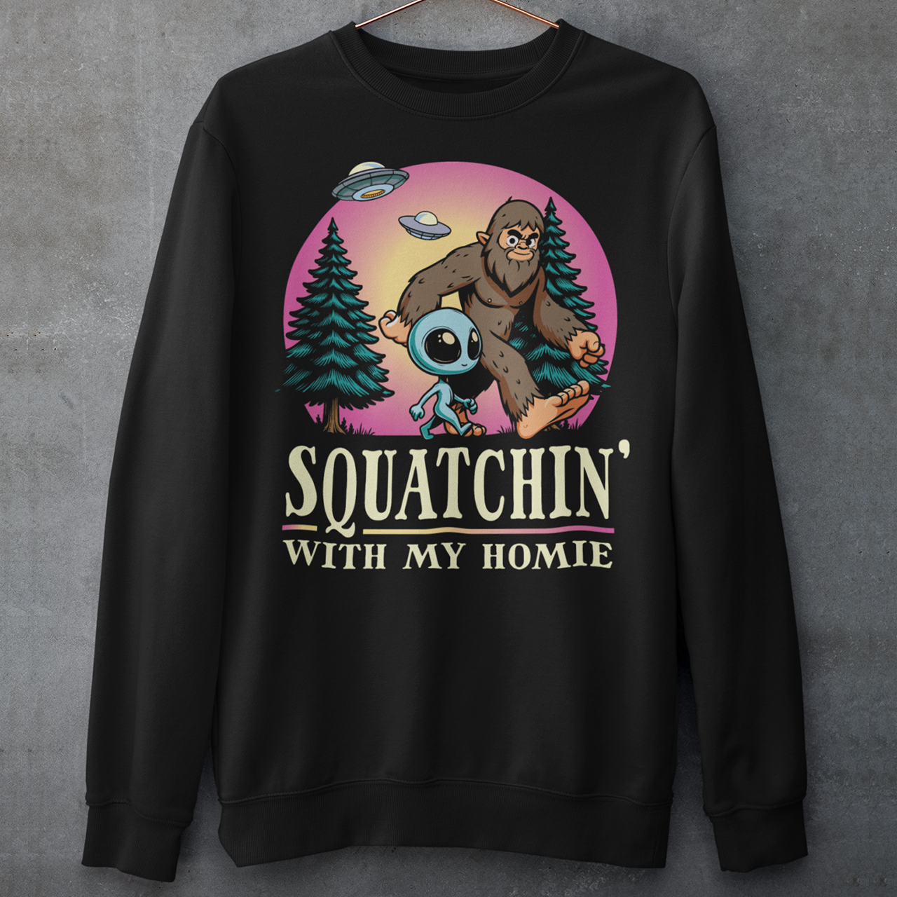 Black sweatshirt of Bigfoot hiking with an alien in the woods with UFOs in the sky with text underneath SQUATCHIN WITH MY HOMIE.