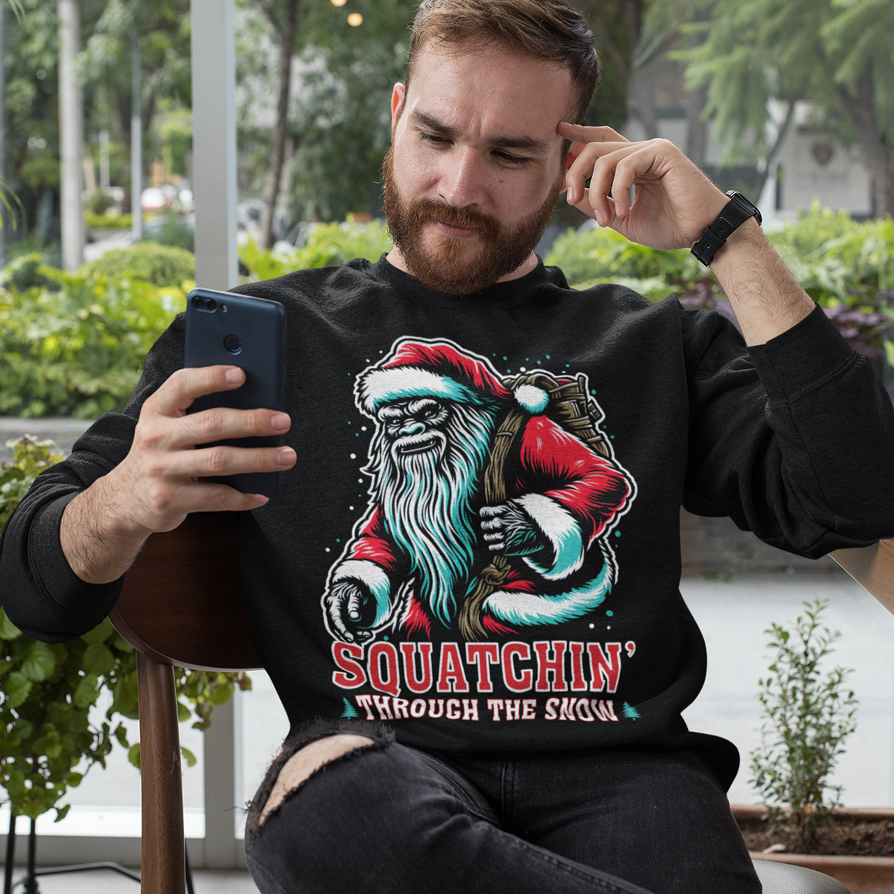 Black Christmas sweatshirt of a Santa sasquatch and text "Squatchin' through the snow."