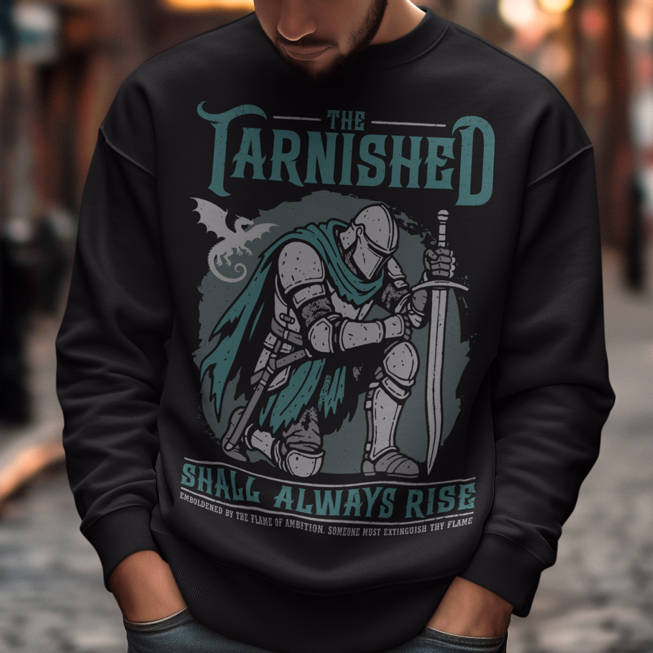 Black sweatshirt featuring a dark fantasy design of a kneeling armored knight holding a sword with teal accents and a dragon silhouette in the background. Large text reads “The Tarnished Shall Always Rise,” with smaller medieval-style text underneath. Inspired by fantasy RPG and soulslike gaming aesthetics.