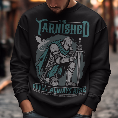 Black sweatshirt featuring a dark fantasy design of a kneeling armored knight holding a sword with teal accents and a dragon silhouette in the background. Large text reads “The Tarnished Shall Always Rise,” with smaller medieval-style text underneath. Inspired by fantasy RPG and soulslike gaming aesthetics.