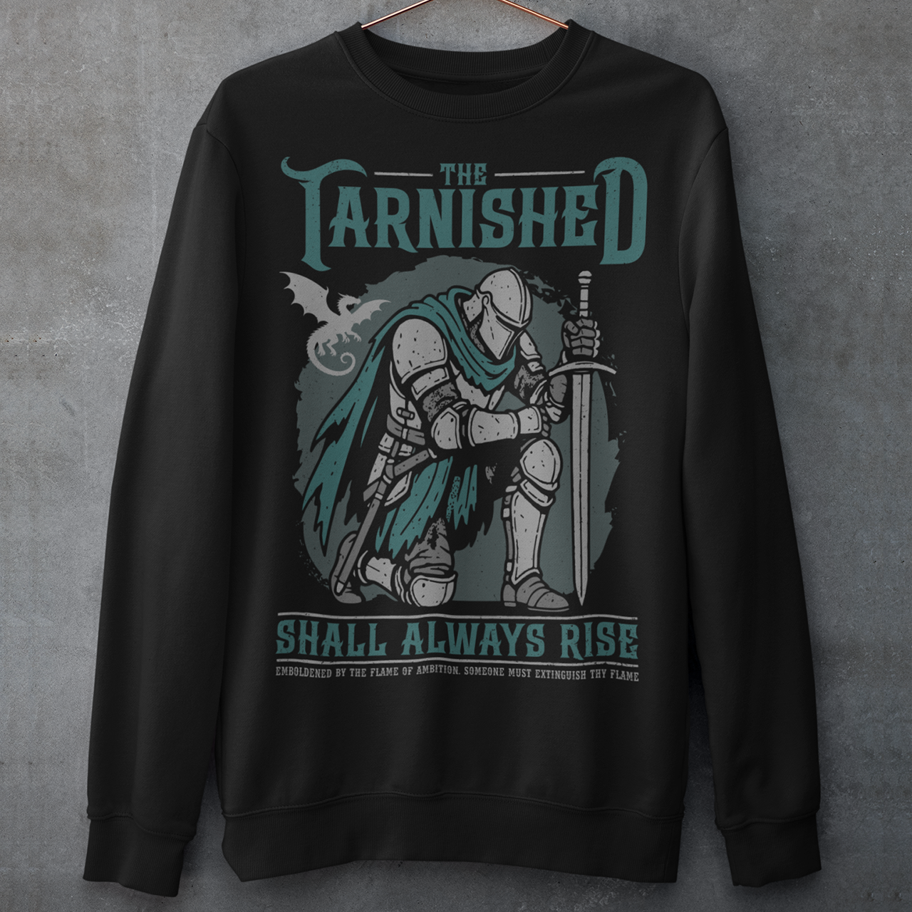 Black sweatshirt featuring a dark fantasy design of a kneeling armored knight holding a sword with teal accents and a dragon silhouette in the background. Large text reads “The Tarnished Shall Always Rise,” with smaller medieval-style text underneath. Inspired by fantasy RPG and soulslike gaming aesthetics.
