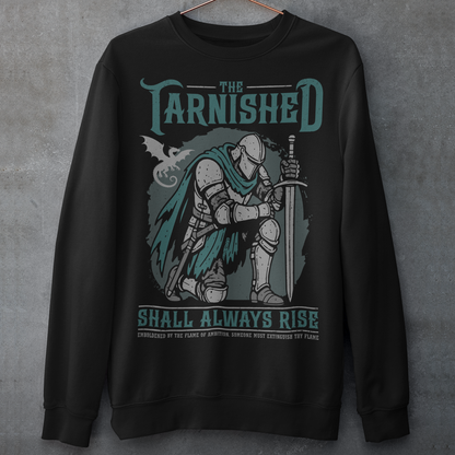 Black sweatshirt featuring a dark fantasy design of a kneeling armored knight holding a sword with teal accents and a dragon silhouette in the background. Large text reads “The Tarnished Shall Always Rise,” with smaller medieval-style text underneath. Inspired by fantasy RPG and soulslike gaming aesthetics.