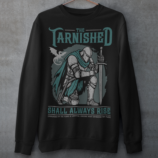 Black sweatshirt featuring a dark fantasy design of a kneeling armored knight holding a sword with teal accents and a dragon silhouette in the background. Large text reads “The Tarnished Shall Always Rise,” with smaller medieval-style text underneath. Inspired by fantasy RPG and soulslike gaming aesthetics.