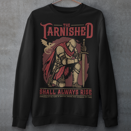 Black sweatshirt featuring a dark fantasy design of a kneeling armored knight holding a sword with redaccents and a dragon silhouette in the background. Large text reads “The Tarnished Shall Always Rise,” with smaller medieval-style text underneath. Inspired by fantasy RPG and soulslike gaming aesthetics.