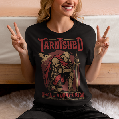 Black t-shirt featuring a dark fantasy design of a kneeling armored knight holding a sword with red accents and a dragon silhouette in the background. Large text reads “The Tarnished Shall Always Rise,” with smaller medieval-style text underneath. Inspired by fantasy RPG and soulslike gaming aesthetics.