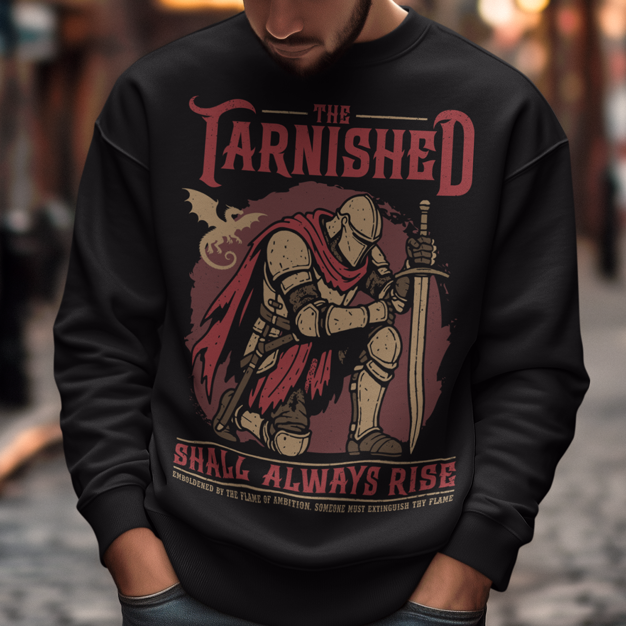 Black sweatshirt featuring a dark fantasy design of a kneeling armored knight holding a sword with redaccents and a dragon silhouette in the background. Large text reads “The Tarnished Shall Always Rise,” with smaller medieval-style text underneath. Inspired by fantasy RPG and soulslike gaming aesthetics.