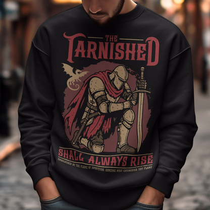 Black sweatshirt featuring a dark fantasy design of a kneeling armored knight holding a sword with redaccents and a dragon silhouette in the background. Large text reads “The Tarnished Shall Always Rise,” with smaller medieval-style text underneath. Inspired by fantasy RPG and soulslike gaming aesthetics.