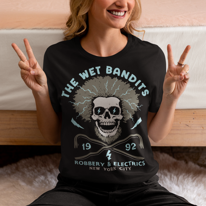 Shock your style to life with this “The Wet Bandits – Robbery And Electrics” t-shirt! Featuring a bold skull design with wild electric hair, crossed crowbars, and vintage lettering, this tee blends rock-n-roll attitude with classic movie nostalgia. Inspired by the unforgettable duo from the holiday favorite, it’s perfect for fans who love edgy humor and retro vibes.