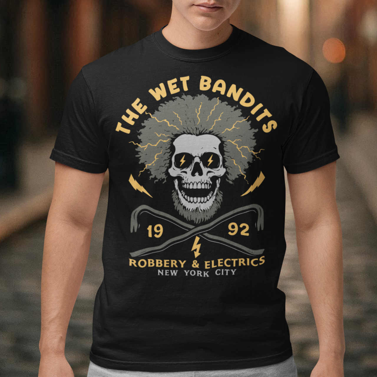 Shock your style to life with this “The Wet Bandits – Robbery &amp; Electrics” t-shirt! Featuring a bold skull design with wild electric hair, crossed crowbars, and vintage lettering, this tee blends rock-n-roll attitude with classic movie nostalgia. Inspired by the unforgettable duo from the holiday favorite, it’s perfect for fans who love edgy humor and retro vibes.