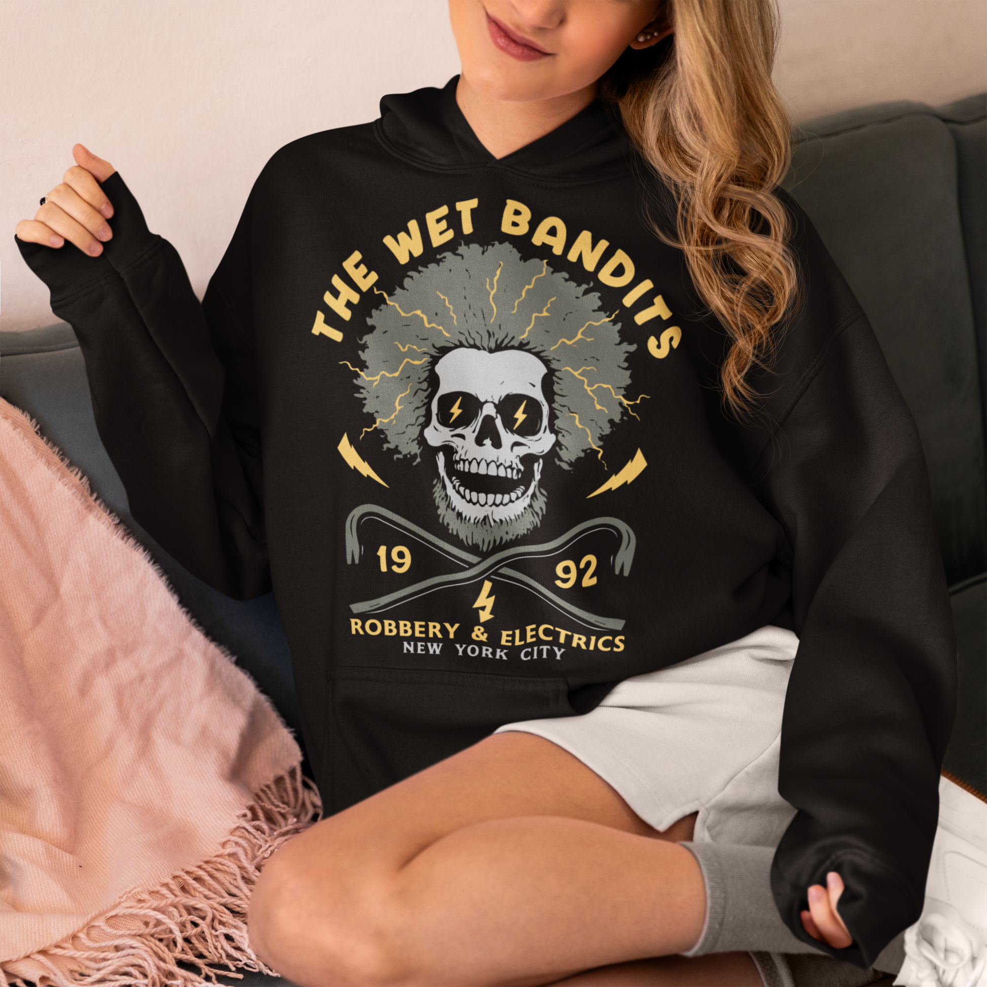 Shock your style to life with this “The Wet Bandits – Robbery And Electrics” hoodie! Featuring a bold skull design with wild electric hair, crossed crowbars, and vintage lettering, this tee blends rock-n-roll attitude with classic movie nostalgia. Inspired by the unforgettable duo from the holiday favorite, it’s perfect for fans who love edgy humor and retro vibes.