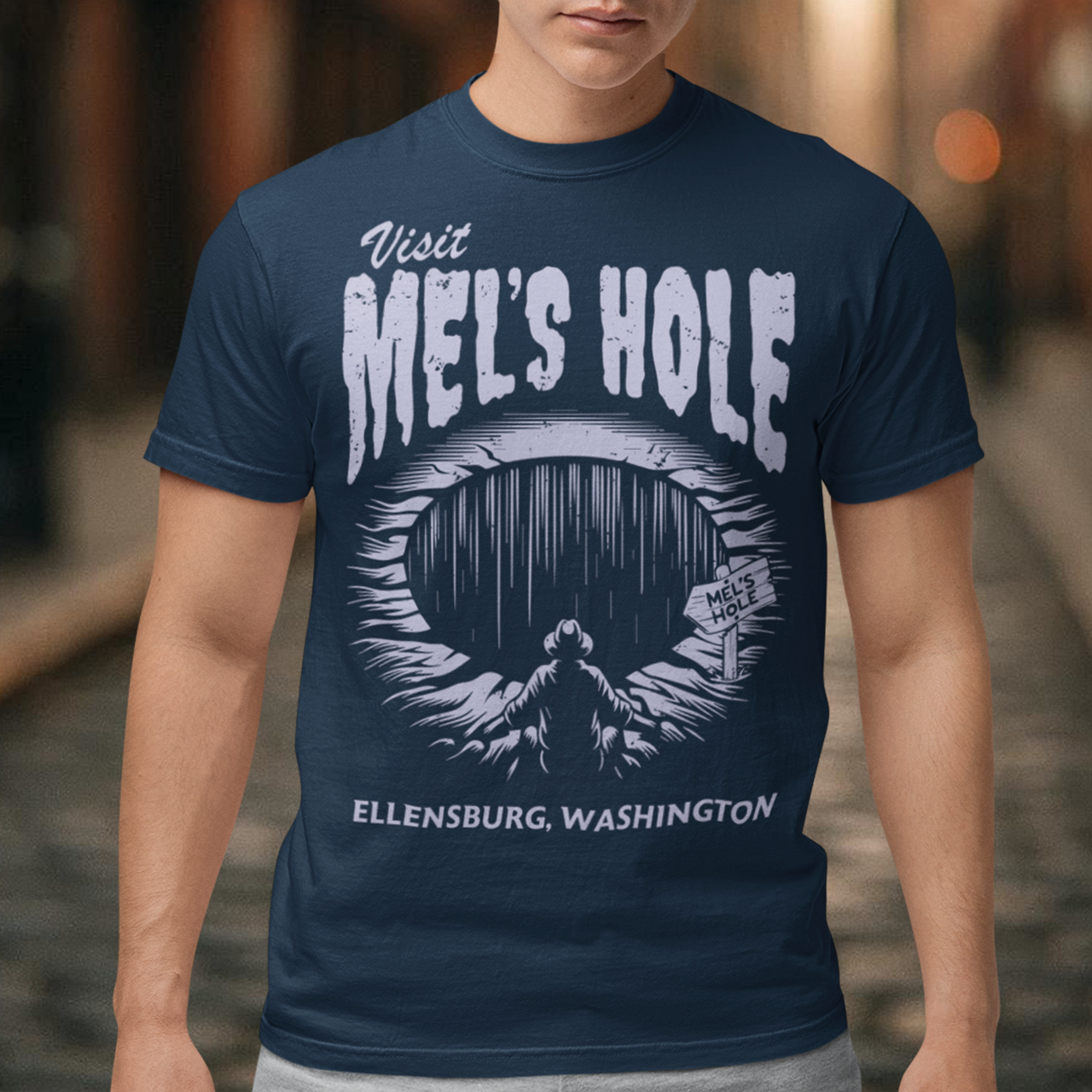 Step into the strange with this quirky and mysterious tee! Featuring a bold illustration of a curious man peering into a dark, bottomless abyss, this shirt pays homage to the legendary paranormal tale of Mel's Hole — a supposed infinite pit in the wilds of Washington State. The vintage-style artwork is topped with the eerie invitation: "VISIT MEL'S HOLE" in retro tourism font, blending humor, folklore, and a dash of the unexplained.