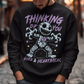 Dark humor meets twisted sweetness with this bold sweatshirt. Featuring a stitched-up voodoo doll at the center, the design captures that perfect mix of love and pain. Above the doll, the phrase “THINKING OF YOU” adds a playful sting, while below, “HUGS &amp; HEARTBREAK” ties it all together with equal parts irony and affection. Perfect for anyone who loves edgy, alternative fashion—or just wants to send a cheeky message without saying a word.